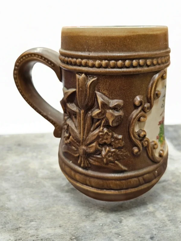 Dekoracyjny kufel ceramiczny z motywem kwiatowym i humorystycznym obrazkiem.