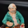 Ręcznie malowana figurka – starszy mężczyzna na ławce z butelką – ceramika, wys. 20 cm