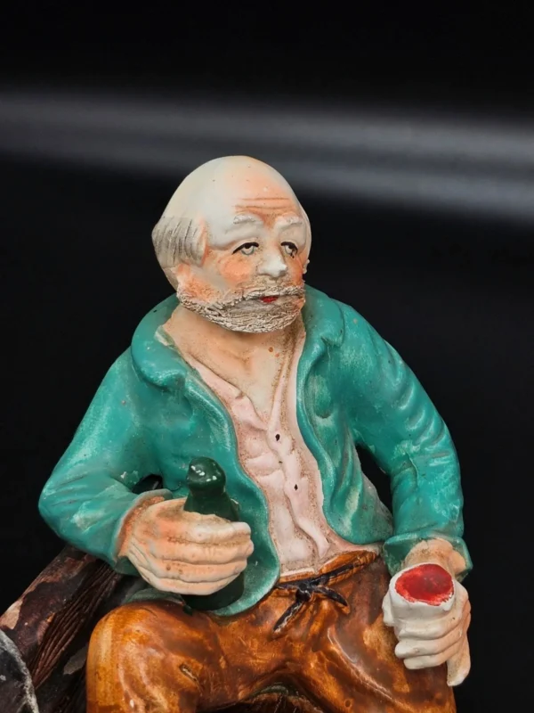 Ręcznie malowana figurka – starszy mężczyzna na ławce z butelką – ceramika, wys. 20 cm